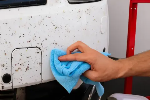 Mano limpiando el coche para quitar mosquitos y restos de insectos.