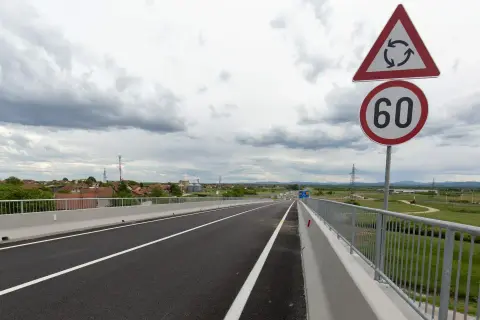 Señal de tráfico indica velocidad minima en carretera convencional de 60 km/h, con un cruce de rotonda cercano.