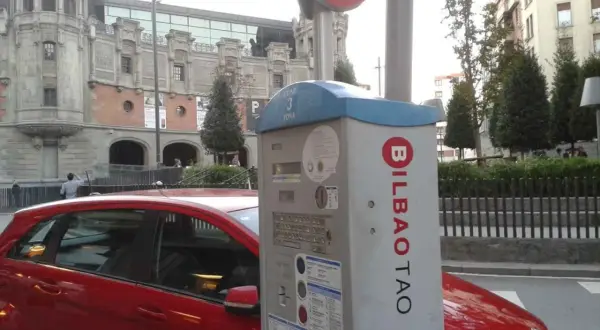Máquina de parquímetro con el logo de BILBAO TAO en una calle de Bilbao. Un coche rojo está aparcado al lado.