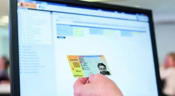 Mano sostiene DNI español frente a pantalla de ordenador con interfaz de apoderamiento DGT.