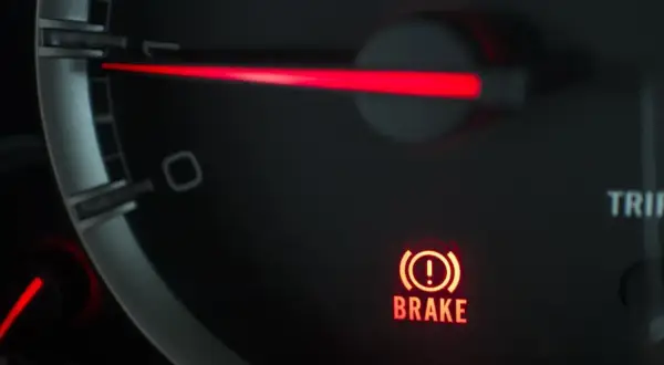 El panel de un coche muestra una luz de advertencia roja con un signo de exclamación dentro de un círculo y la palabra "BRAKE". Esto indica que algo no va bien con el sistema de frenos.