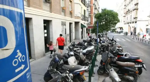 Señal azul de normativa aparcamiento motos. Calle con muchas motos aparcadas y un padre con su hija caminando.