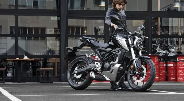 Joven con chaqueta de cuero junto a una moto negra. ¡Si te sacas el carnet de coche puedes conducir moto!