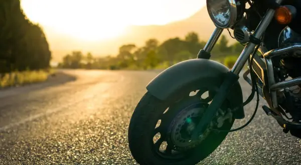 Rueda delantera de una motocicleta en una carretera al atardecer. La tija de la moto se ve claramente, lista para el viaje.