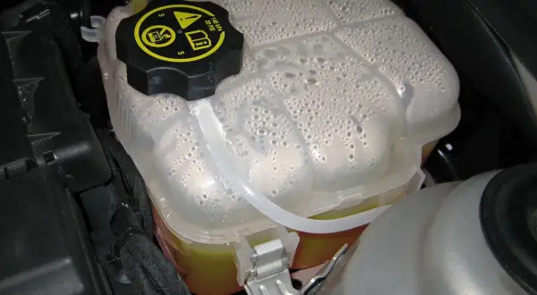 Depósito de expansión con líquido refrigerante y burbujas. Es hora de rellenar líquido refrigerante para mantener el motor fresco.