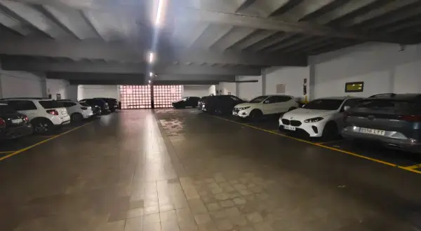 Coches aparcados en diagonal en un garaje subterráneo con iluminación fluorescente y suelo de baldosas.