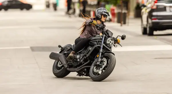 Mujer con casco y chaqueta de cuero conduce una motocicleta negra. Sorprendentemente, una motocicleta puede circular sin tubo de escape, demostrando su potencia.