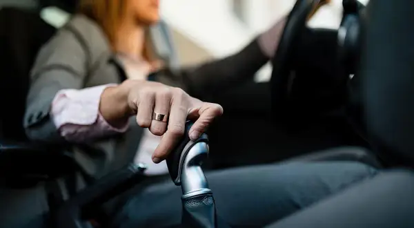 Mano con anillo sobre palanca de cambios, aprendiendo como conducir un coche automático.