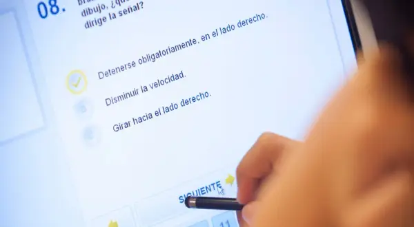 Persona realizando el test DGT A1 en una pantalla táctil. La pregunta 8, con una opción marcada, se centra en la señalización.