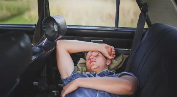 Joven duerme en el asiento trasero de un coche, con una brizna de hierba en la cara. Se puede dormir en el coche en un viaje largo.