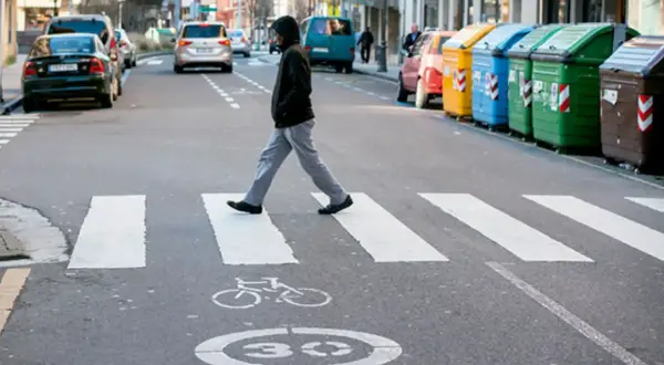 Un hombre cruza la calle por un paso de cebra. Se considera peatón a la persona que camina, y él está haciendo exactamente eso, respetando las normas de tráfico.