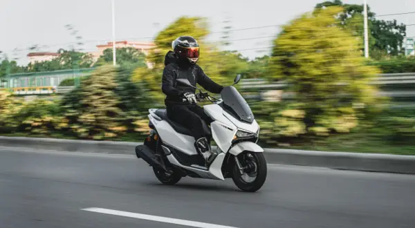 Persona con casco y chaqueta negra conduce una moto blanca. La edad para conducir moto de 125cc es 16 años.