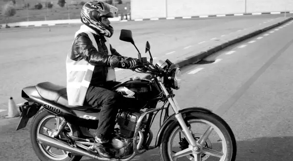Motociclista con casco y chaleco reflectante en un circuito, preparándose para un test am dgt.