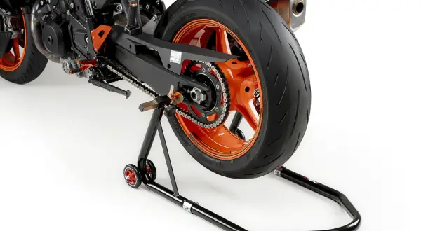 La rueda trasera de una moto deportiva naranja está elevada sobre un caballete basculante negro.