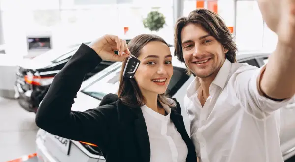 Pareja feliz celebrando la compra de un coche nuevo, ella muestra las llaves. ¡Ya pueden poner el coche a nombre de dos personas!
