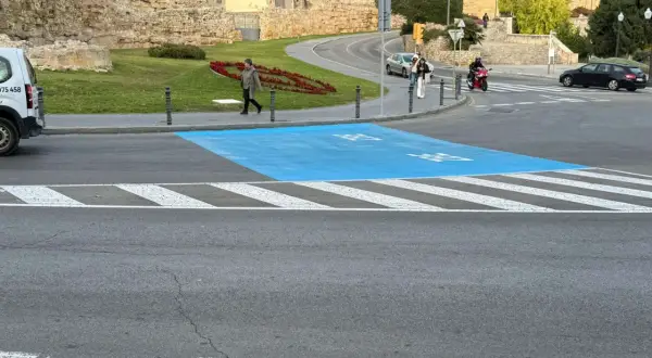 Paso de peatones azul en la zona bajas emisiones de Tarragona, con restos arqueológicos al fondo.