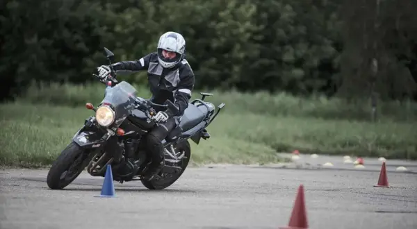 Motociclista en entrenamiento, practicando maniobras para obtener su **permiso a**. Conos marcan el circuito.
