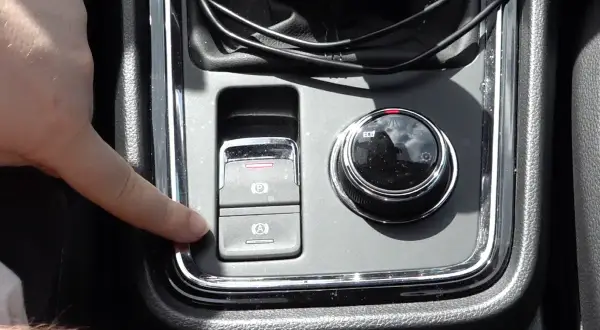 Dedo presionando el botón de freno de mano electrónico en un coche. Esto es útil para entender qué significa "hold" en un coche, ya que activa el freno automático.