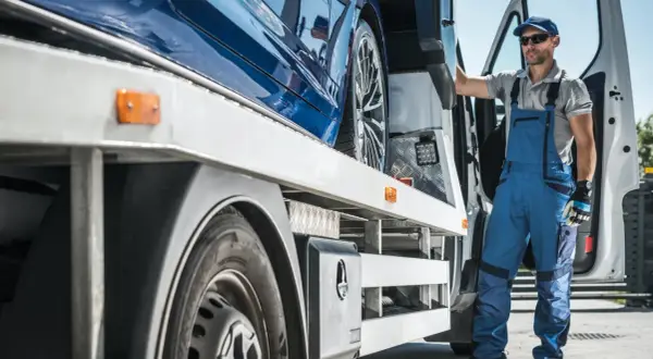 Trabajador con mono azul junto a un coche azul en una grúa. Un paso más para saber como quitar el embargo de un coche.