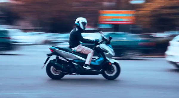 Motorista en moto 125cc, con casco blanco, circulando rápido. La imagen evoca la libertad de movimiento, quizás pensando en la nueva normativa motos 125.