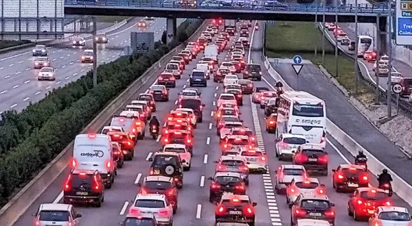 Motociclista aprovecha el atasco para adelantar con moto en autopista congestionada. Coches parados, luces rojas y un autobús blanco.