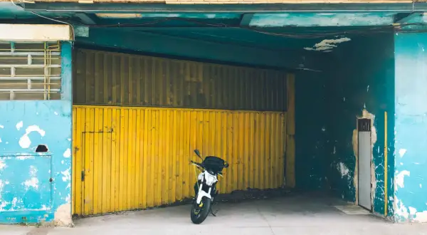 Una moto blanca espera en una cochera con puerta amarilla, donde se puede aparcar sin vado.