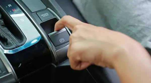 Dedo presionando el botón del freno de estacionamiento eléctrico, junto a la palanca de cambios.