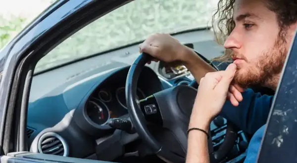 Hombre con barba y pelo rizado, pensativo, con la mano en la barbilla, dentro de un coche. Se escucha un ruido clack clack al girar el volante en parado.
