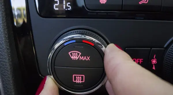 Dedo girando el dial para desempañar cristales coche. Muestra la temperatura 21.5 y el icono de desempañado.