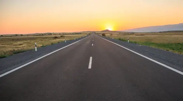 Una carretera convencional se extiende hacia el horizonte bajo un atardecer dorado.