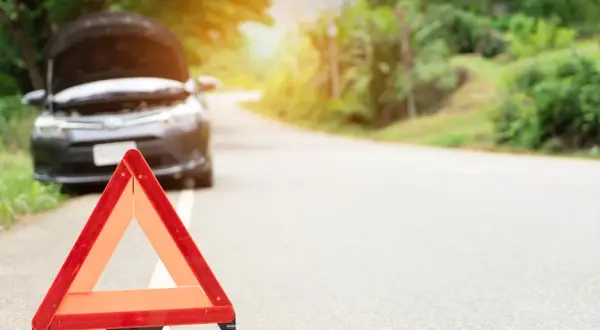 Triángulo de emergencia rojo en el arcén. El capó de un coche está abierto, indicando una avería.