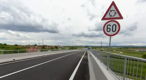 Señal de tráfico indica velocidad minima en carretera convencional de 60 km/h, con un cruce de rotonda cercano.