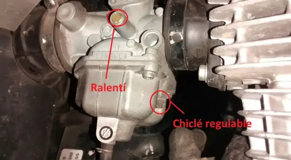 Detalle de carburador de moto, mostrando el tornillo de ralentí y el chiclé regulable.