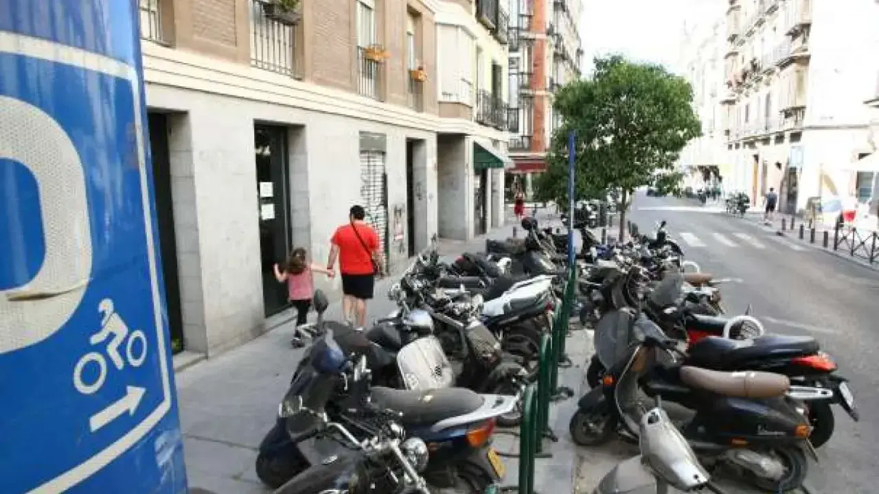 Señal azul de normativa aparcamiento motos. Calle con muchas motos aparcadas y un padre con su hija caminando.