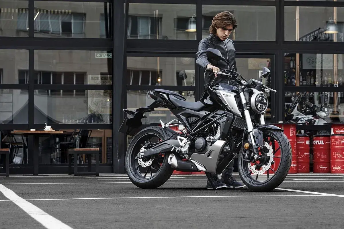 Joven con chaqueta de cuero junto a una moto negra. ¡Si te sacas el carnet de coche puedes conducir moto!