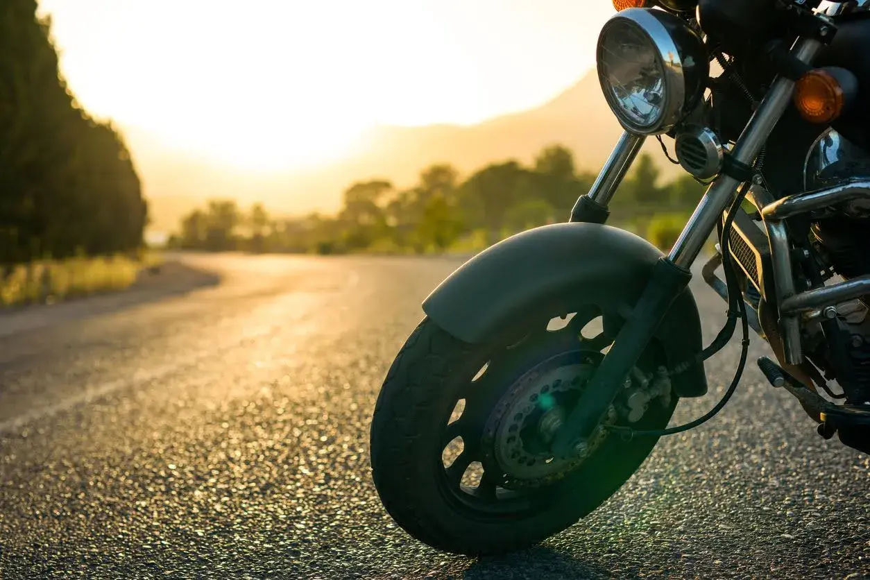 Rueda delantera de una motocicleta en una carretera al atardecer. La tija de la moto se ve claramente, lista para el viaje.