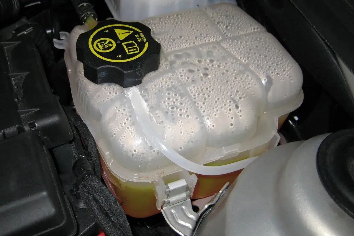 Depósito de expansión con líquido refrigerante y burbujas. Es hora de rellenar líquido refrigerante para mantener el motor fresco.