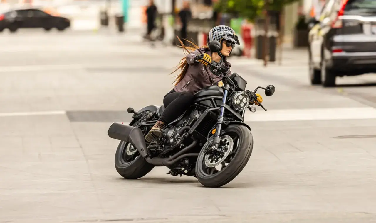 Mujer con casco y chaqueta de cuero conduce una motocicleta negra. Sorprendentemente, una motocicleta puede circular sin tubo de escape, demostrando su potencia.