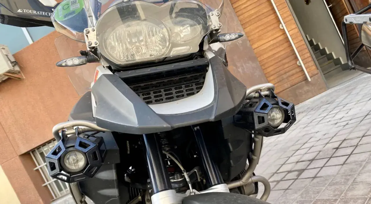 Detalle frontal de una motocicleta con dos luces antiniebla hexagonales negras montadas en los laterales.