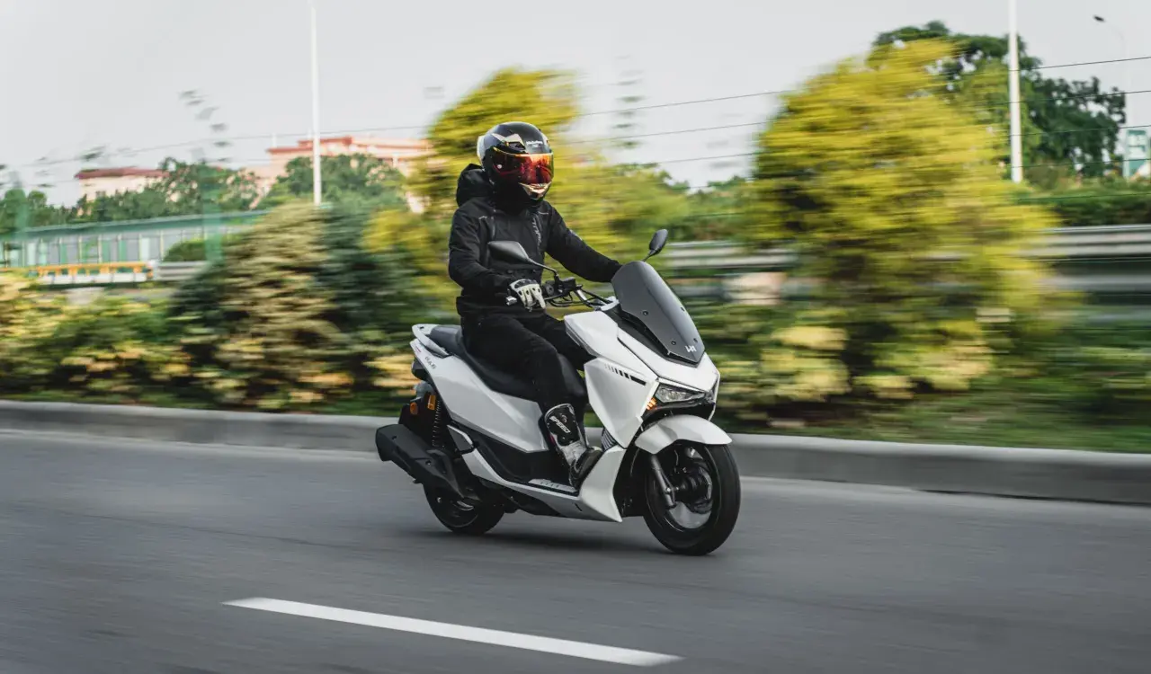 Persona con casco y chaqueta negra conduce una moto blanca. La edad para conducir moto de 125cc es 16 años.