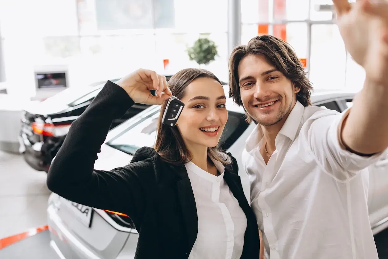 Pareja feliz celebrando la compra de un coche nuevo, ella muestra las llaves. ¡Ya pueden poner el coche a nombre de dos personas!