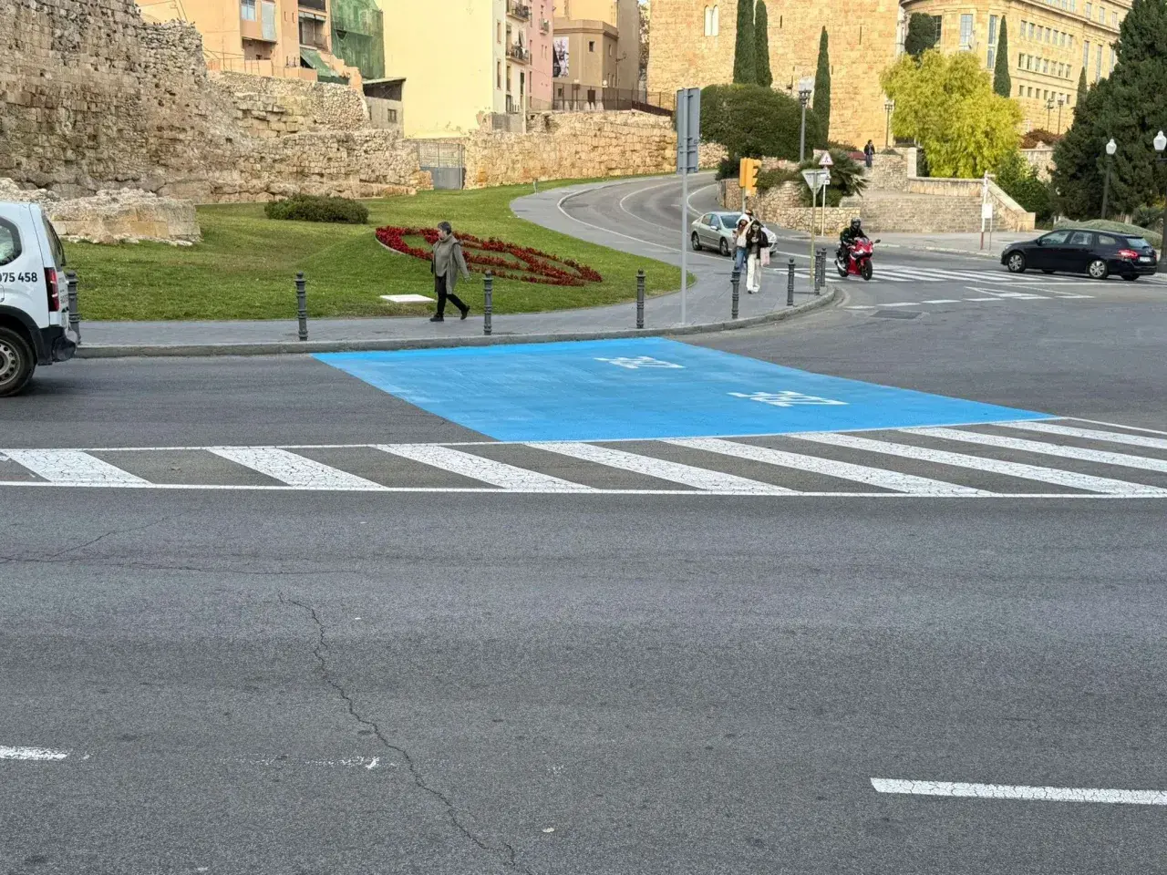 Paso de peatones azul en la zona bajas emisiones de Tarragona, con restos arqueológicos al fondo.