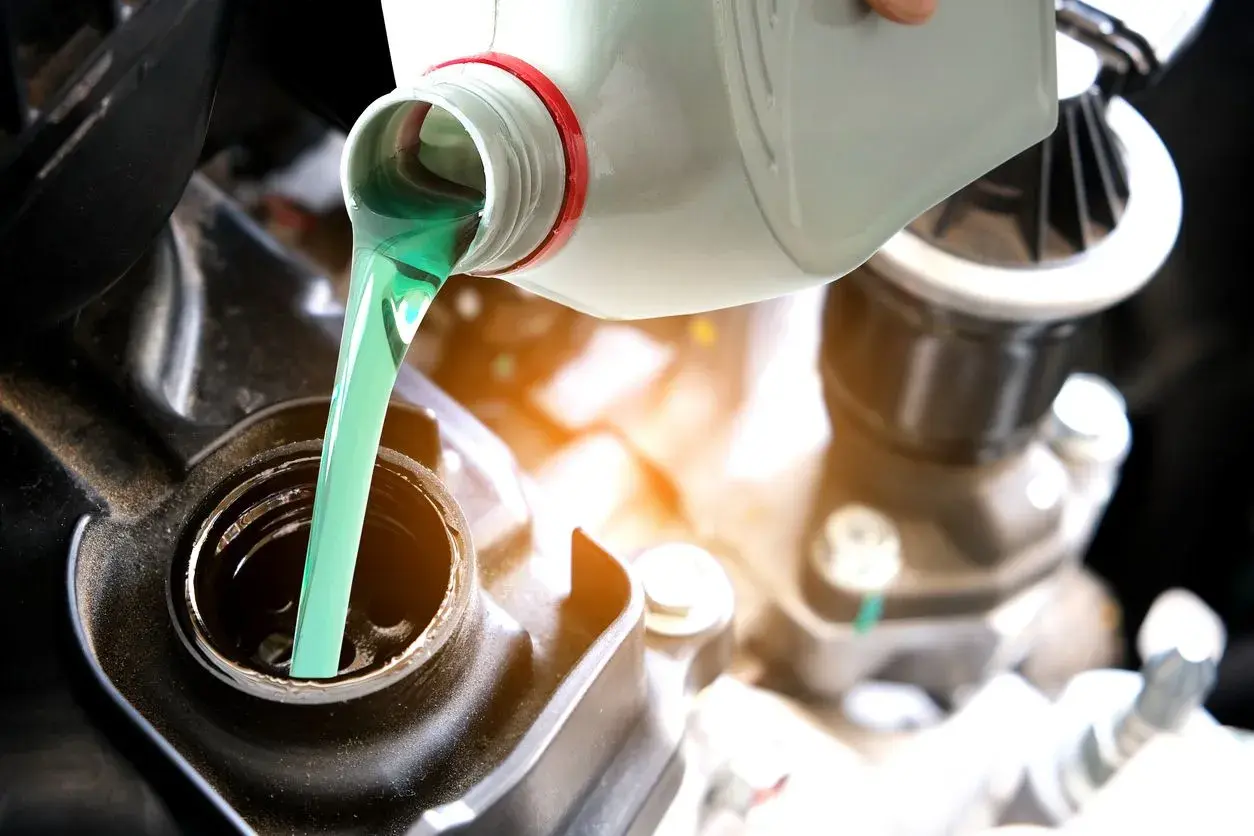 Vertiendo aceite 2T verde brillante en el motor de una motocicleta. El correcto porcentaje aceite 2t es crucial para el rendimiento.