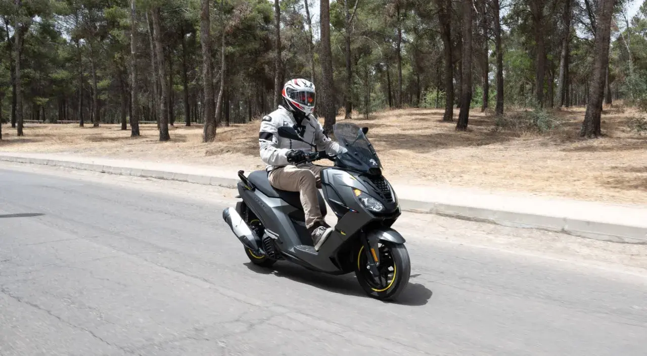 Hombre con casco conduce moto Peugeot con carnet B por carretera rodeada de pinos.