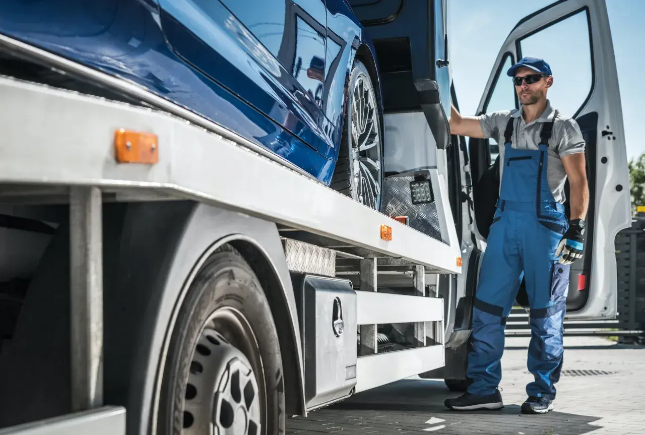 Trabajador con mono azul junto a un coche azul en una grúa. Un paso más para saber como quitar el embargo de un coche.