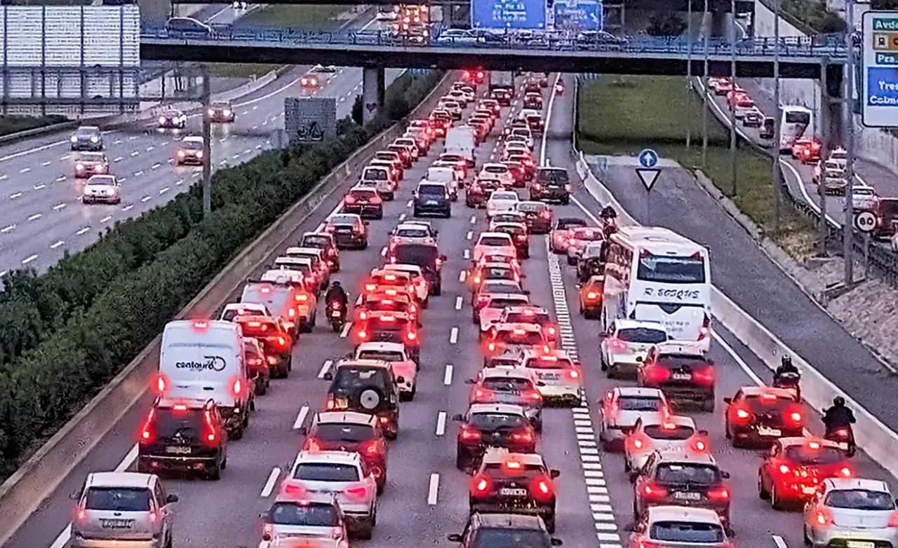 Motociclista aprovecha el atasco para adelantar con moto en autopista congestionada. Coches parados, luces rojas y un autobús blanco.