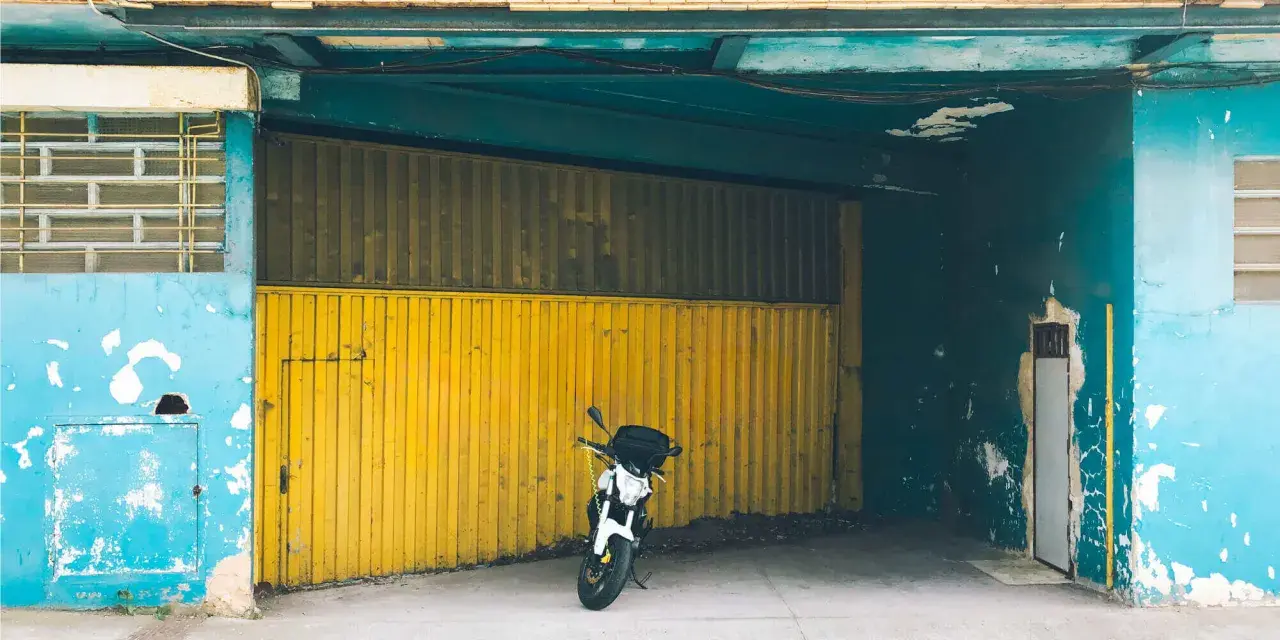 Una moto blanca espera en una cochera con puerta amarilla, donde se puede aparcar sin vado.