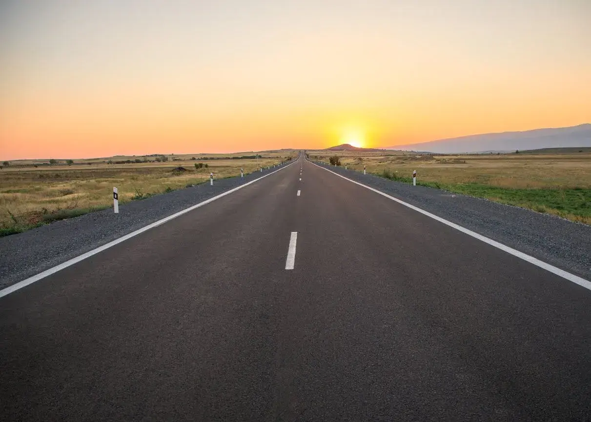 Una carretera convencional se extiende hacia el horizonte bajo un atardecer dorado.