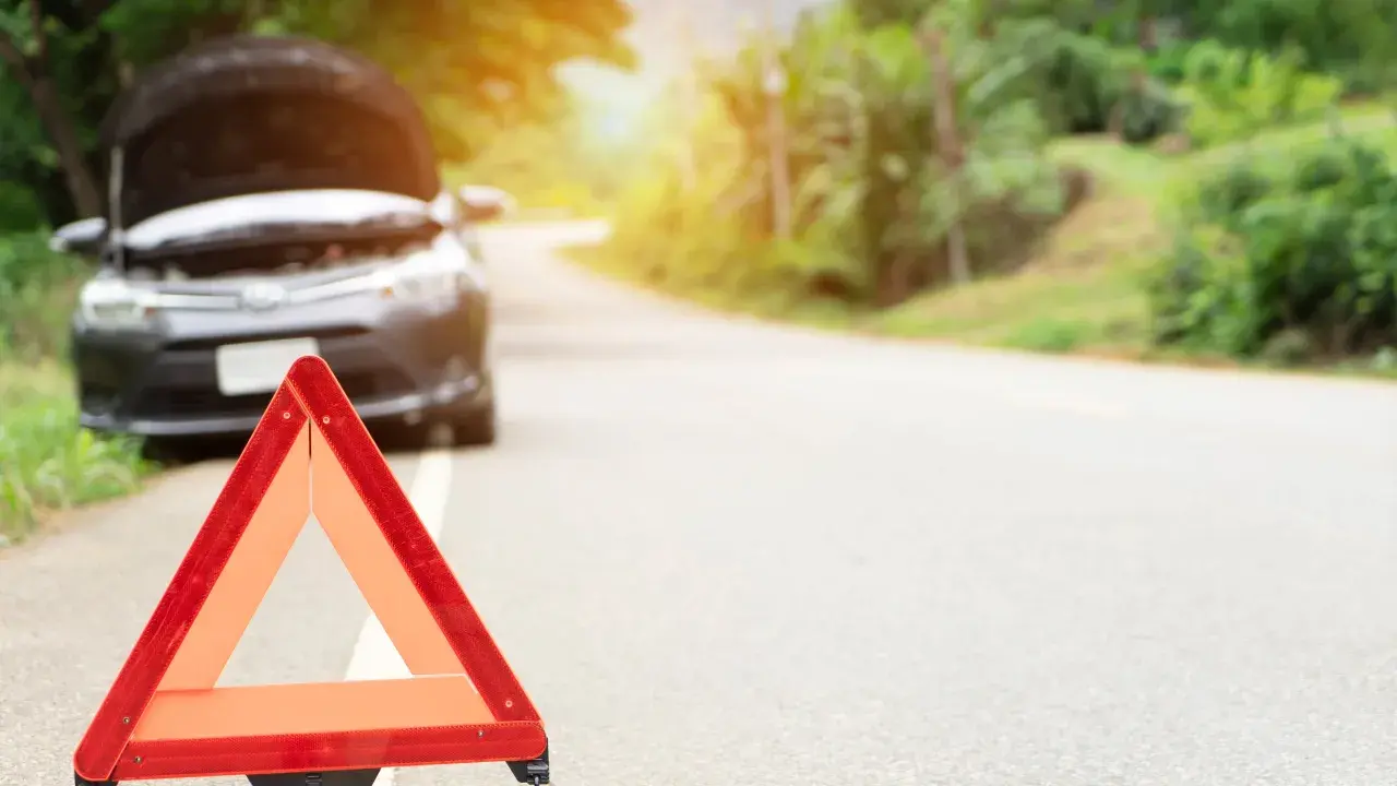 Triángulo de emergencia rojo en el arcén. El capó de un coche está abierto, indicando una avería.