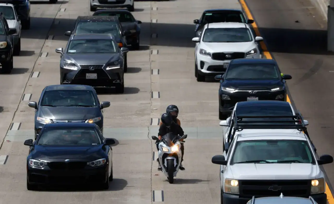 Dos personas en moto logran adelantar con moto en atasco, esquivando coches parados en la autopista.
